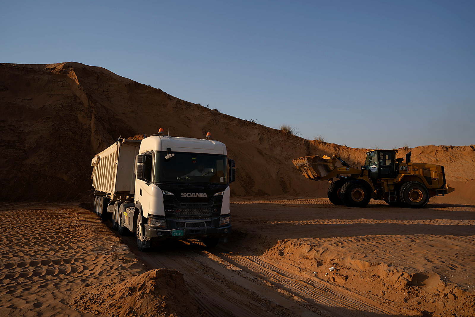 Al Mabar 6-wheel tipper loading against a red dune at golden hour